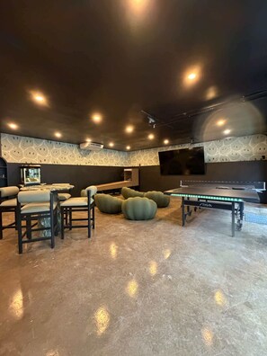 A room with a ping pong table, bean bags, and a pool table.
