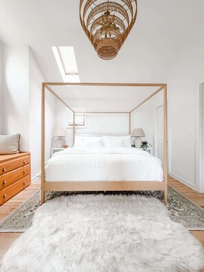 A modern bedroom with a four-poster bed, a fluffy white rug, and a unique woven ceiling light fixture.