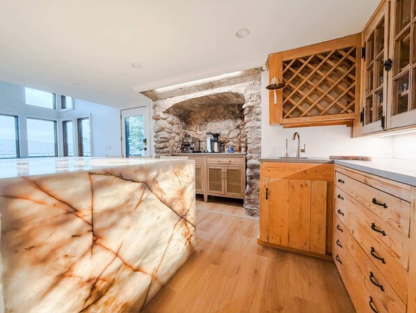 A modern kitchen with stone archway, wooden cabinets, and a marble island.