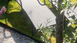 Two outdoor lounge chairs with metal frames and dark cushions, positioned on a grassy area with a stone wall in the background. - Elmalı Guest House 
A simple, serene, and deeply peaceful life awaits you! (Muğla)