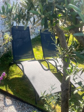 Due poltrone da esterno con struttura in metallo e cuscini scuri, collocate su un prato con un muro in pietra sullo sfondo.