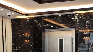 A modern elevator with a metallic finish, a reception desk with a wooden panel, and a marble-patterned wall. - Kalkan Hotel (Istanbul)