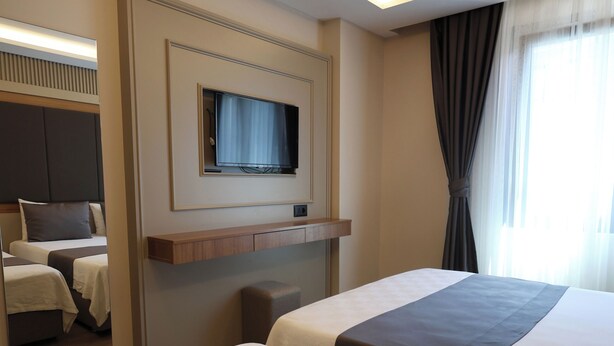 A hotel room with two beds, a television mounted on the wall, and a window with curtains. - Kalkan Hotel (Istanbul)