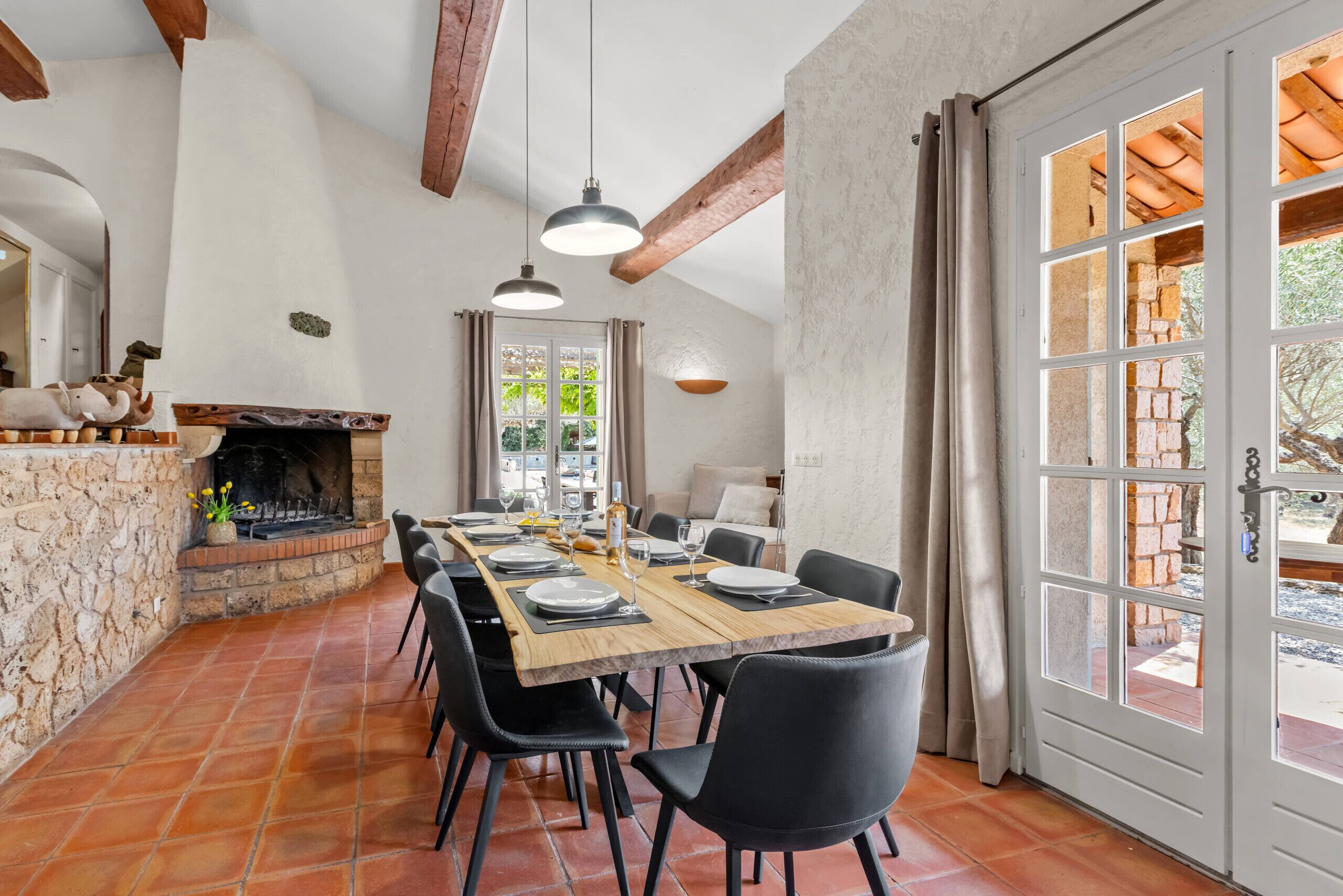 A dining area with a long wooden table, black chairs, and a stone fireplace.