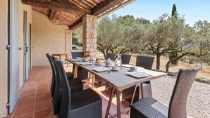 Zona de menjador exterior coberta amb una taula per a quatre persones, envoltada de cadires de vimet i sota una pérgola de fusta.