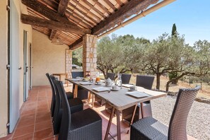 A covered outdoor dining area with a table set for four, surrounded by wicker chairs, under a wooden pergola. - Villa Cococinel by Sur la mer (Salernes)