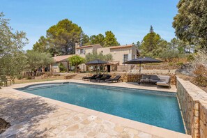 A swimming pool with lounge chairs and umbrellas, surrounded by stone walls and trees. - Villa Cococinel by Sur la mer (Salernes)