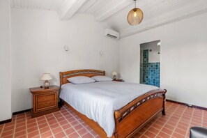 A bedroom with a wooden bed, two bedside tables with lamps, a wall-mounted air conditioner, and a tiled floor. - Villa Cococinel by Sur la mer (Salernes)