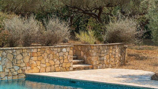 Una piscina de pedra amb aigua turquesa, envoltada per una paret de pedra i vegetació natural.