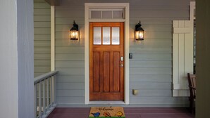 A wooden front door with a glass panel, flanked by two wall-mounted lanterns, and a welcome mat with bird illustrations. - The Perch - Big Canoe, GA (Big Canoe)
