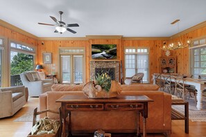 A spacious living room with a fireplace, wooden walls, and a ceiling fan.