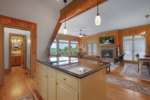 A spacious kitchen with a large island, wooden ceiling beams, and a stone fireplace.