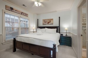 A bedroom with a bed, two bedside tables, a ceiling fan, and artwork on the walls.