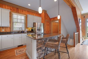 A kitchen with wooden paneling, a stone backsplash, a stainless steel refrigerator, and a bar area with wicker chairs. - The Perch - Big Canoe, GA (Big Canoe)