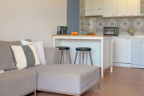 A modern living room with a grey sofa, two bar stools, a kitchen area with a toaster, and a white cabinet. - Sea View over Portisco Bay - Spacious 3BR Home - Clima (Porto Rotondo)