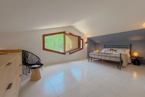 Ein Schlafzimmer mit Bett, Nachttisch, Lampe und Blick ins Grüne durch ein Fenster.