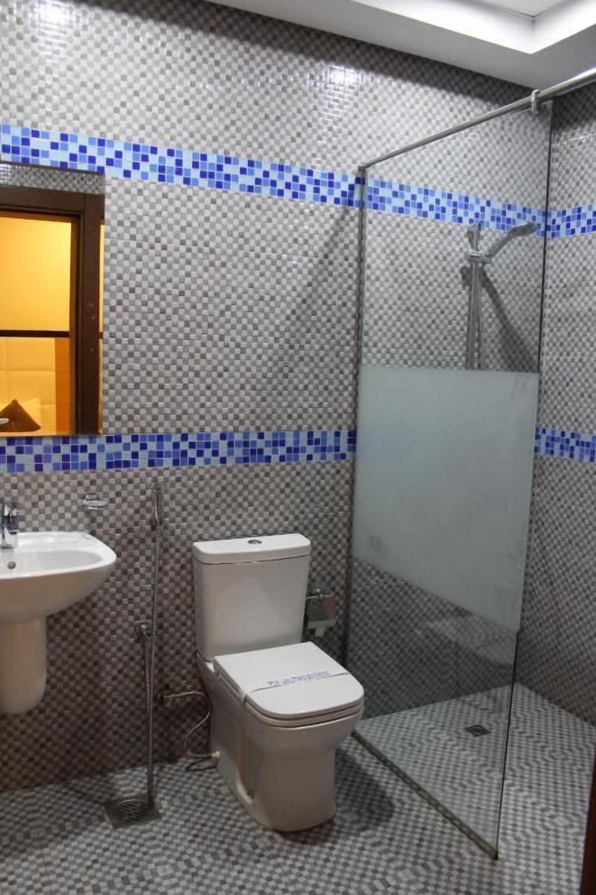 Un baño con pared de azulejos, un lavamanos, un inodoro y una cabina de ducha.