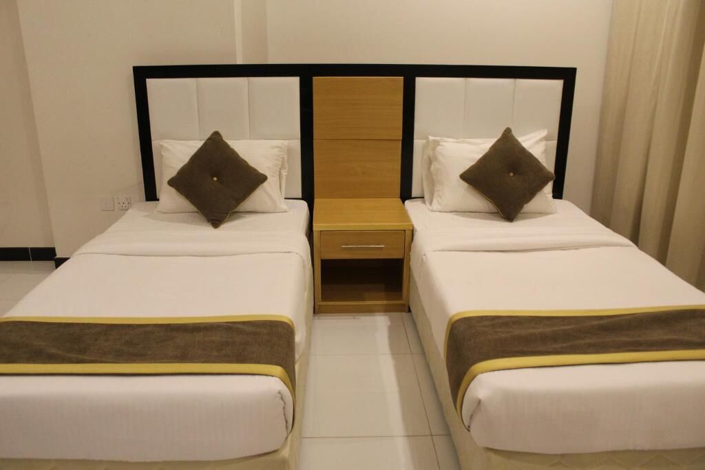 Habitación de hotel con dos camas individuales, cabecera de madera y una mesita de noche pequeña.