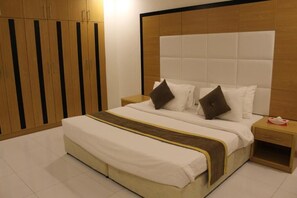 Een hotelkamer met een groot bed, een houten garderobe en een nachtkastje met een zakdoosje.