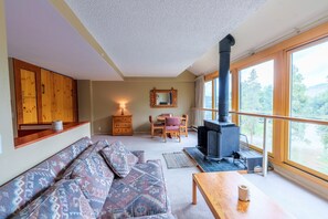 A cozy living room with a sofa, a wooden cabinet, a dresser, a table, a chair, a fireplace, and large windows offering a view of the outdoors. - 1811 Decatur Condo (Keystone)