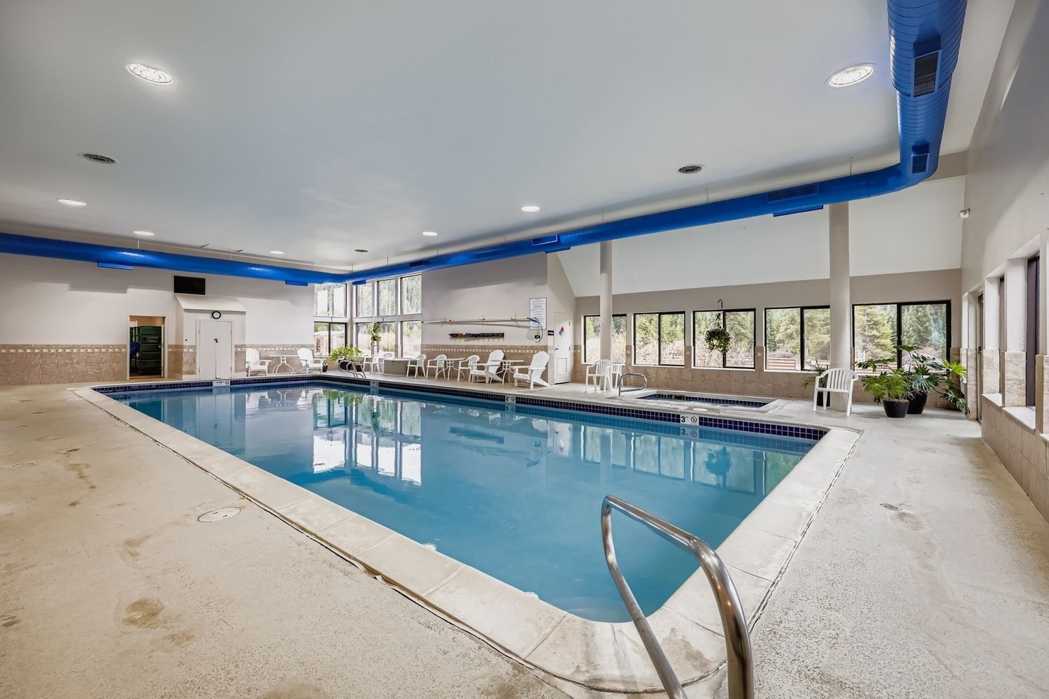 A large indoor swimming pool with a diving board, surrounded by windows and seating areas.