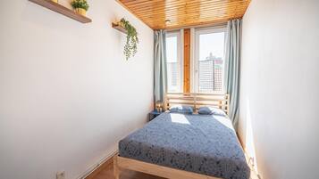Une chambre avec un plafond en bois, un lit recouvert d’une couvre-lit à motifs, deux tables de chevet et une fenêtre avec des rideaux.
