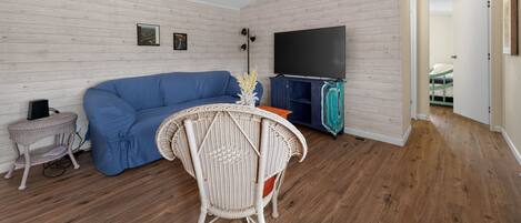 Ein Wohnzimmer mit einem blauen Sofa, einem weißen Rattan-Sessel, einem Flachbildfernseher und einem Deckenventilator.