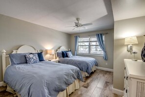 Ein Schlafzimmer mit zwei Betten, einem Deckenventilator, einem Fenster mit Vorhängen und einer Nachttischlampe.