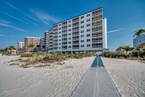 Een hotel aan het strand met meerdere verdiepingen, een overdekte gang en een zandstrand.