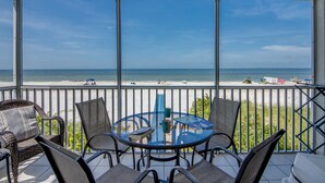 A balcony with a glass table and chairs overlooking a beach. - Beach Villas 101 Beachfront Condo: Heated Pool, Walk To Dwtn 2 Bedroom Condo (Fort Myers Beach)