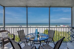 Ein Balkon mit Glastisch und Stühlen mit Blick auf einen Strand.