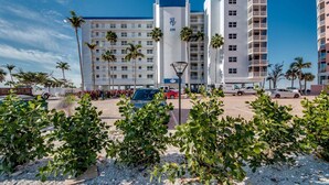 A multi-story hotel with balconies, palm trees, and a parking area. - Beach Villas 101 Beachfront Condo: Heated Pool, Walk To Dwtn 2 Bedroom Condo (Fort Myers Beach)
