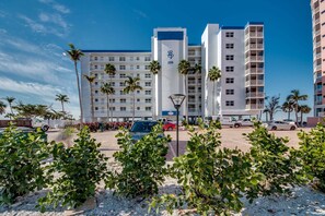 Ein mehrstöckiges Hotel mit Balkonen, Palmen und einem Parkplatz.