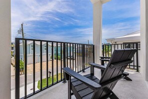 Ein Balkon mit Metallgeländer, zwei Adirondack-Stühle und Blick auf eine Wohngegend.
