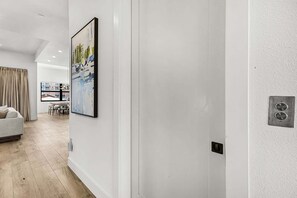 Un pasillo con una puerta blanca, un cuadro abstracto enmarco y una pequeña unidad de ventilación en la pared.