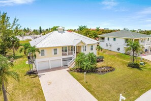 A two-story residential building with a front porch, a garage, and a landscaped yard with palm trees. - 21188 Noddy Tern: 4br Home W/ Pool 4 Bedroom Home (Fort Myers Beach)
