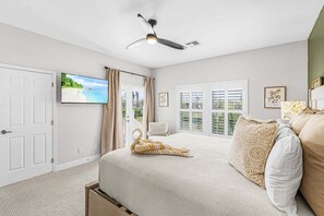 A bedroom with a bed, a ceiling fan, a TV on the wall, and a view of the outdoors through a window. - 21188 Noddy Tern: 4br Home W/ Pool 4 Bedroom Home (Fort Myers Beach)
