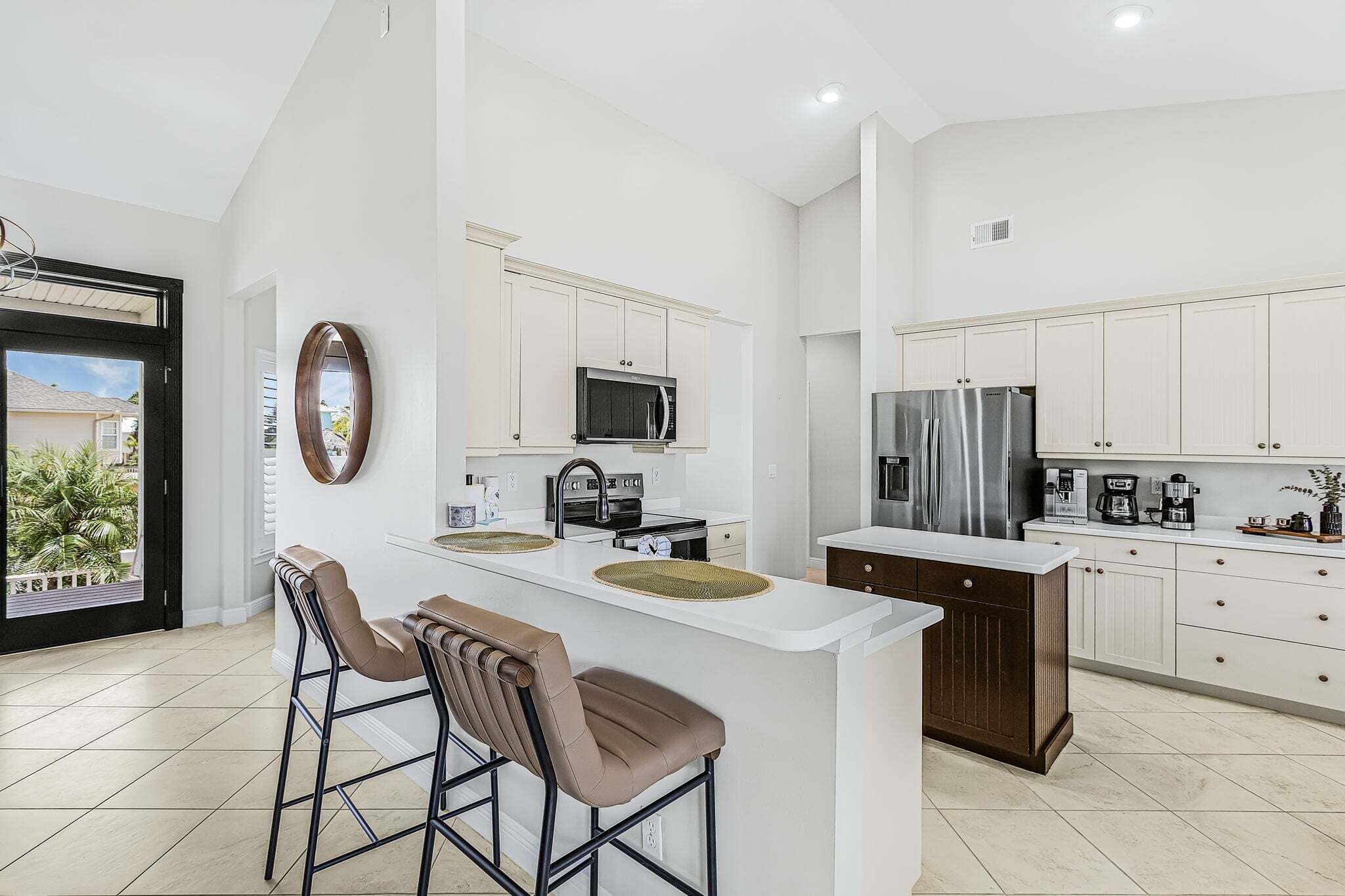 A modern kitchen with a central island, bar stools, a microwave, a stove, a refrigerator, and a coffee maker.