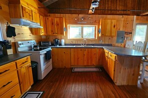 Una cocina tipo cabaña de madera con estufa, pileta y un ventanal grande.