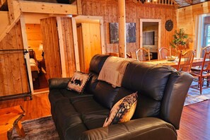 Una sala de estar acogedora con un sofá de cuero, paredes de madera y un comedor con mobiliario de madera.