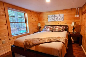 Quarto de cabana de madeira com cama, duas luminárias de cabeceira, uma janela e um letreiro na parede.