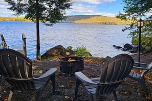A lakeside seating area with Adirondack chairs and a fire pit.