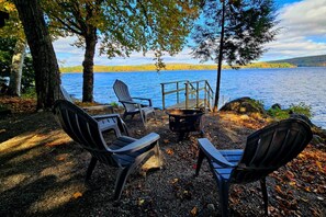 Ein Sitzbereich am Seeufer mit Adirondack-Stühlen und einer Feuerstelle.