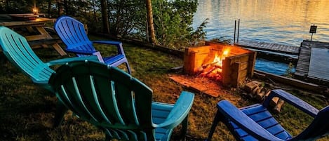 A lakeside outdoor seating area with Adirondack chairs and a fire pit.