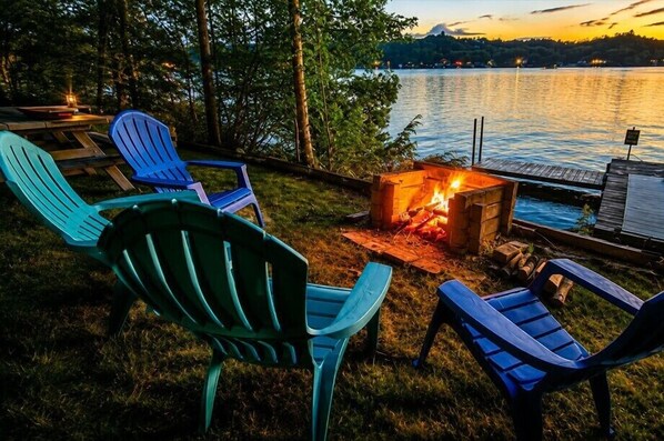 Ein Sitzbereich im Freien am Seeufer mit Adirondack-Stühlen und einer Feuerstelle.