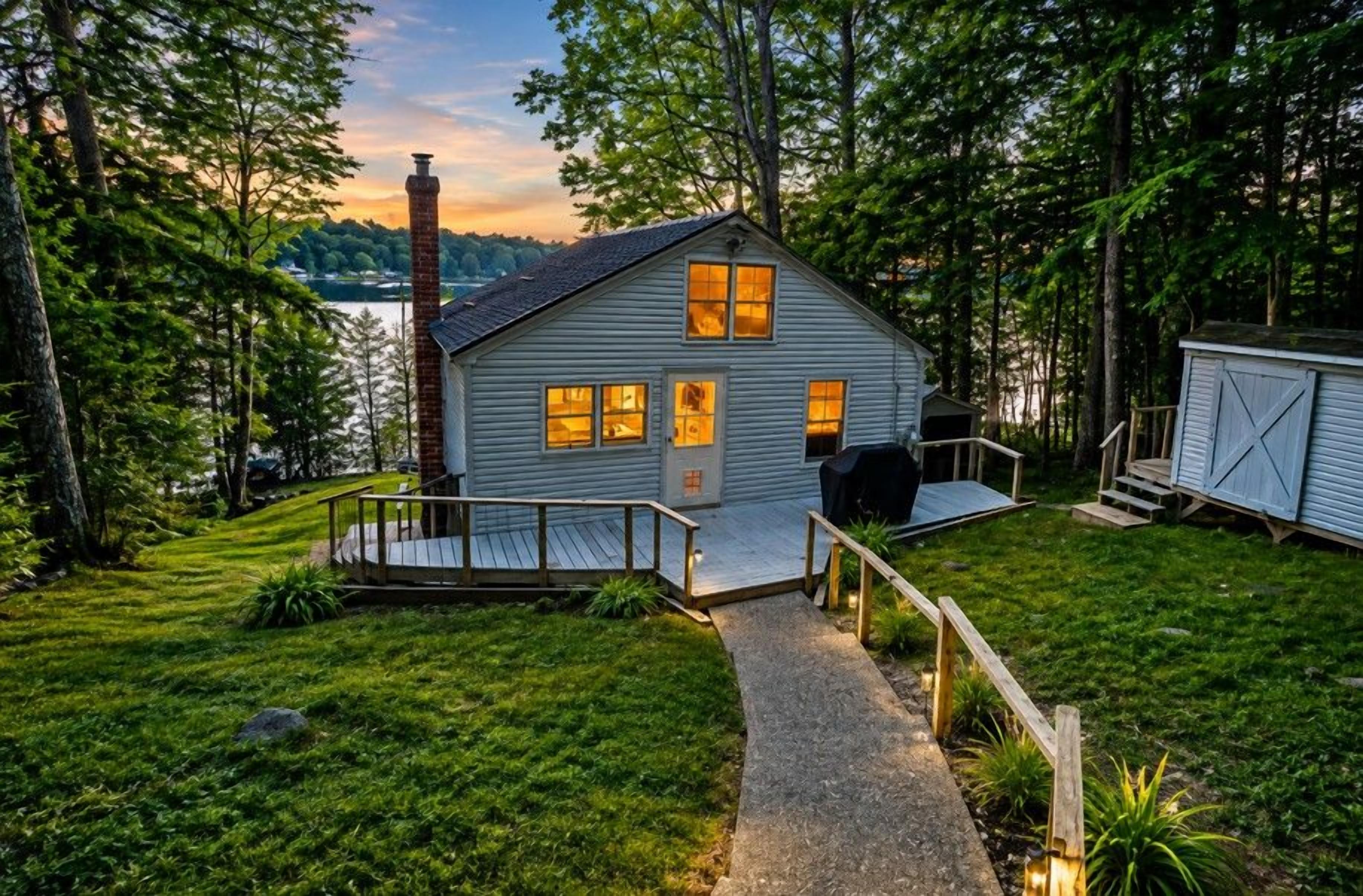 A cabin with a deck, a chimney, and a view of a lake.