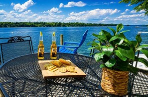 Ein runder Metalltisch mit einer Holzplatte, auf der Fruchtscheiben und Cracker, zwei Corona-Bierflaschen und ein Topfpflanze stehen.