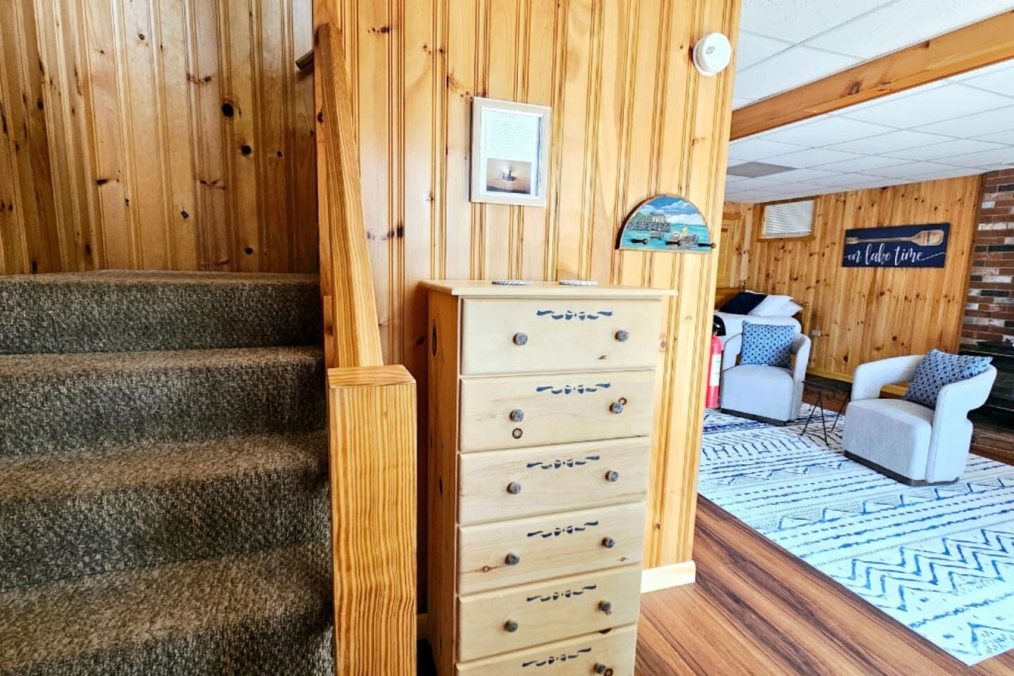 A wooden staircase leading to a room with a wooden chest of drawers, a framed picture, and a sign that says "Live Life."