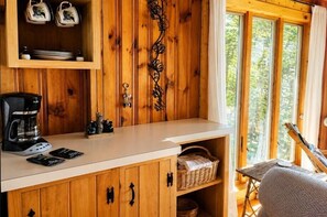 A wooden cabin interior with a kitchenette, a coffee maker, and a view of the outdoors. - Great Pond Getaway|Lakefront|Dock|Sunset Views (Belgrade)