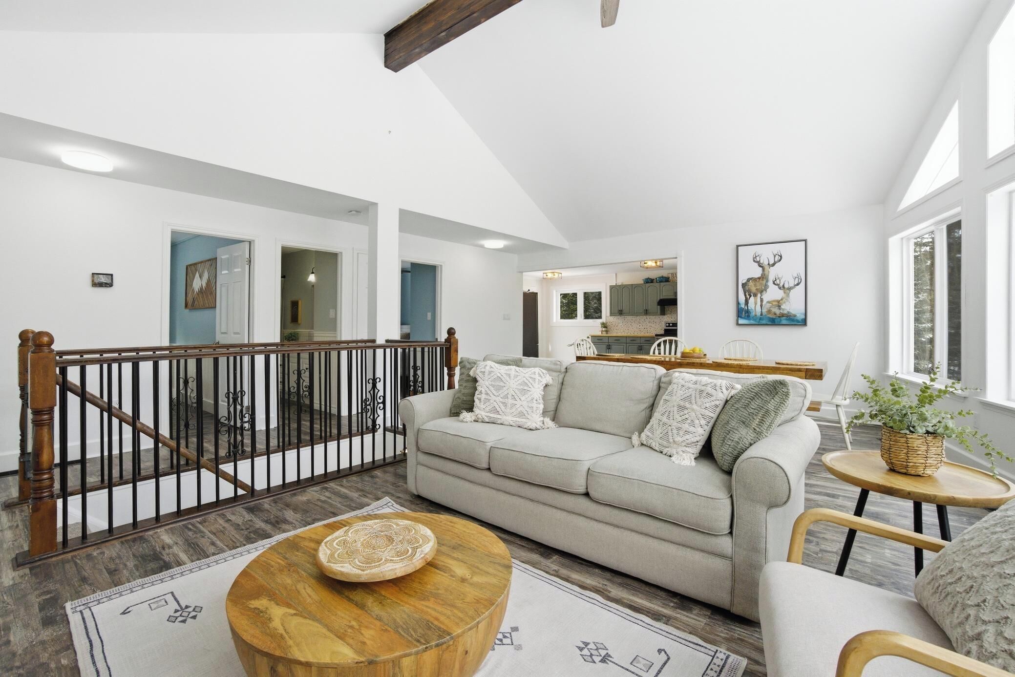A spacious living area with a high ceiling, a staircase, a kitchen in the background, and a large window.